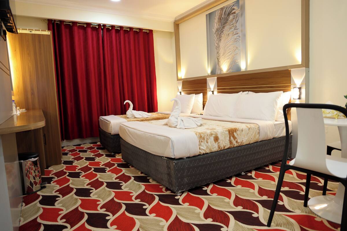 A hotel room with two beds, a red curtain, a wooden headboard, and a patterned carpet.