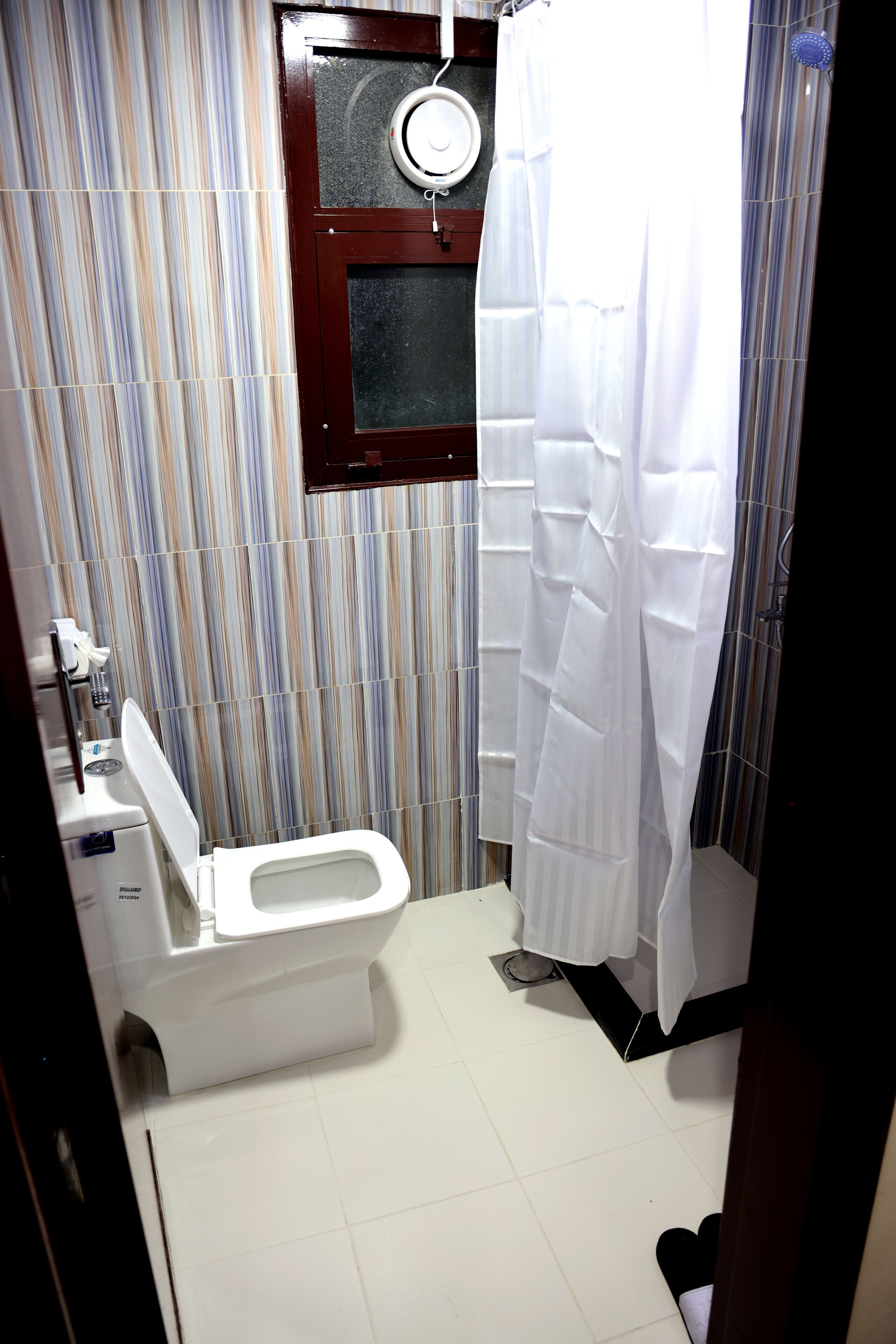 Une salle de bain avec des toilettes, une fenêtre et un rideau de douche.