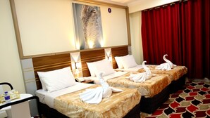 Habitación de hotel con dos camas, cada una con sábanas blancas y una manta dorada, un escritorio con una silla y una cortina roja.