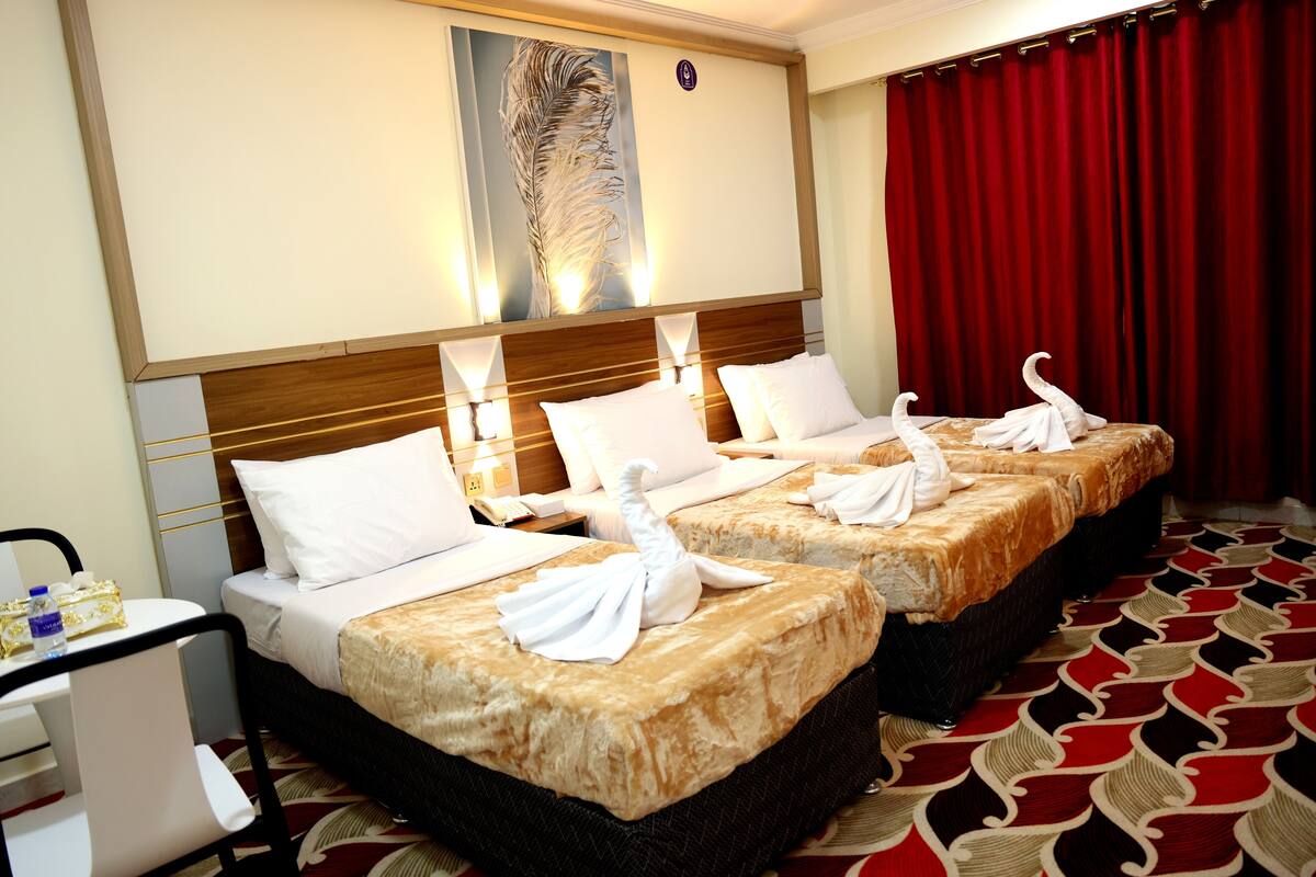 A hotel room with two beds, each with white linens and a golden blanket, a desk with a chair, and a red curtain.