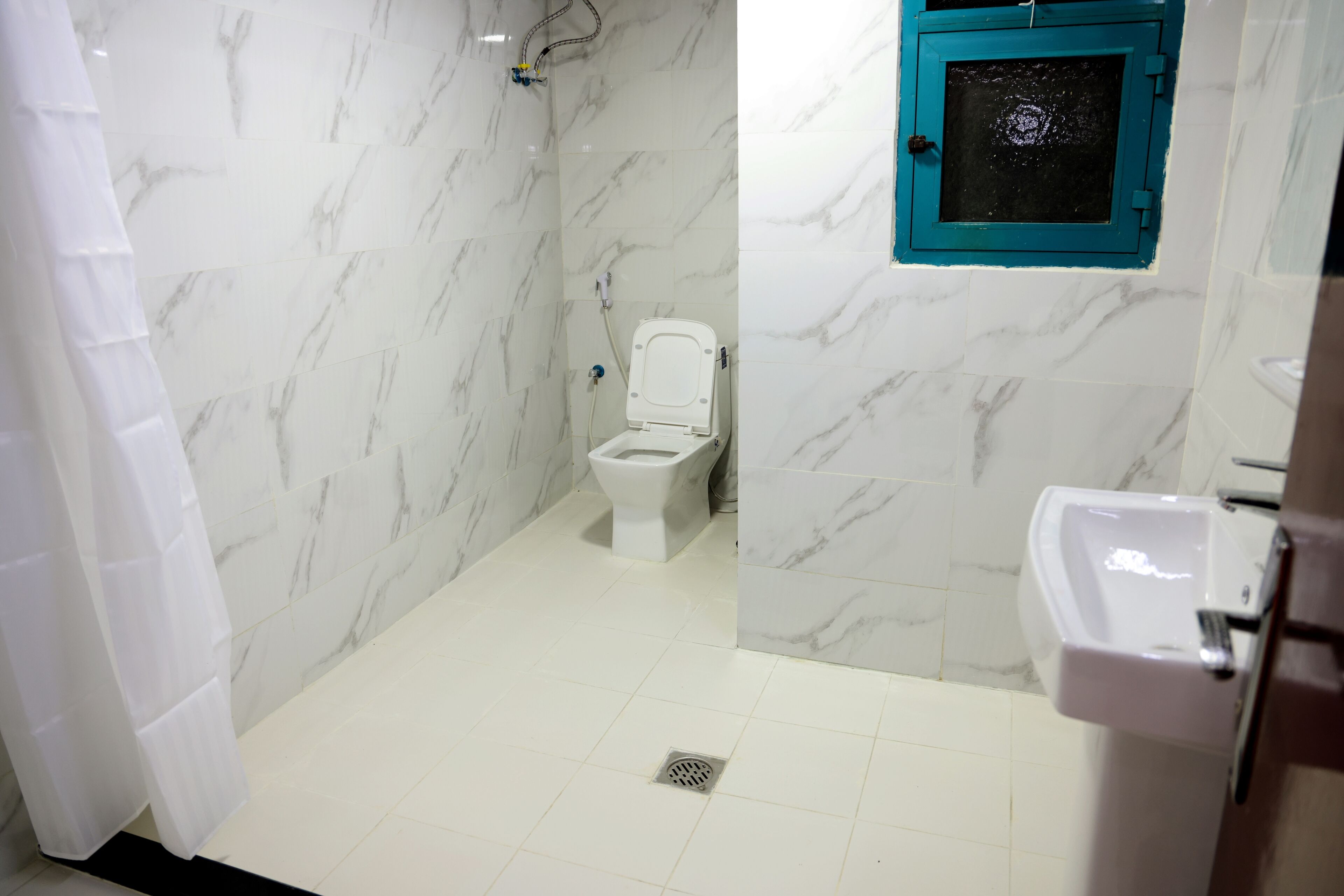A bathroom with white marble tiles, a white toilet, a blue window, and a white sink.