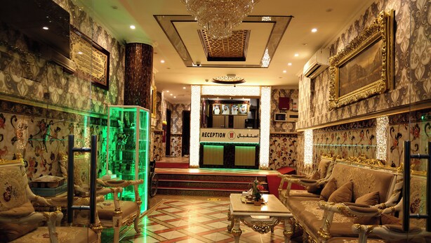 Un hall de lujo con muebles ornamentados, un mostrador de recepción y una vitrina iluminada en verde.