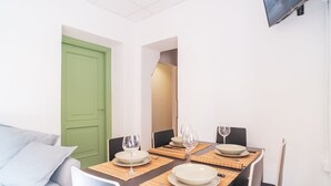 A dining area with a table set for four, chairs, a green door, and a TV mounted on the wall. - BuddyRent - Theo's Trevi - 7 ospiti (Roma)