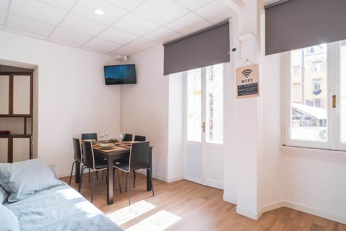 Une pièce comprenant un lit, une table à manger avec des chaises, un téléviseur fixé au mur, une fenêtre donnant sur un paysage agréable et un panneau indiquant la présence d’une connexion Wi-Fi.