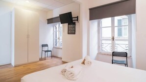 A hotel room with a bed, a chair, a TV mounted on the wall, and a window with a view.