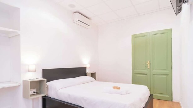 A bedroom with a bed, bedside lamps, a nightstand, a green door, and an air conditioning unit. - BuddyRent - Theo's Trevi - 7 ospiti (Roma)