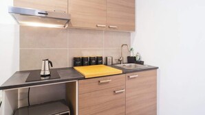 A modern kitchen with wooden cabinets, a black countertop, a stainless steel kettle, a cutting board, and a sink.