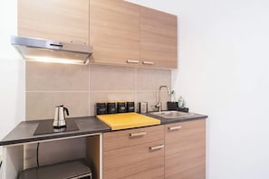 A modern kitchen with wooden cabinets, a black countertop, a stainless steel kettle, a cutting board, and a sink.