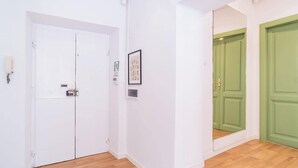 Un pasillo con paredes blancas, suelo de madera y dos puertas, una blanca y otra verde.