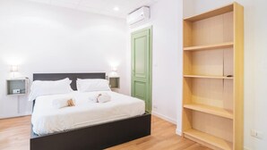 Un dormitorio con cama, mesitas de noche, una puerta verde y una estantería de madera.