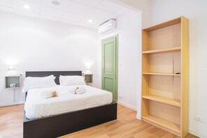 Une chambre à coucher avec un lit, des tables de chevet, une porte verte et une étagère en bois.