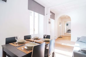 A dining area with a table set for four, a sofa, and a view of a hallway. - BuddyRent - Theo's Trevi - 7 ospiti (Roma)