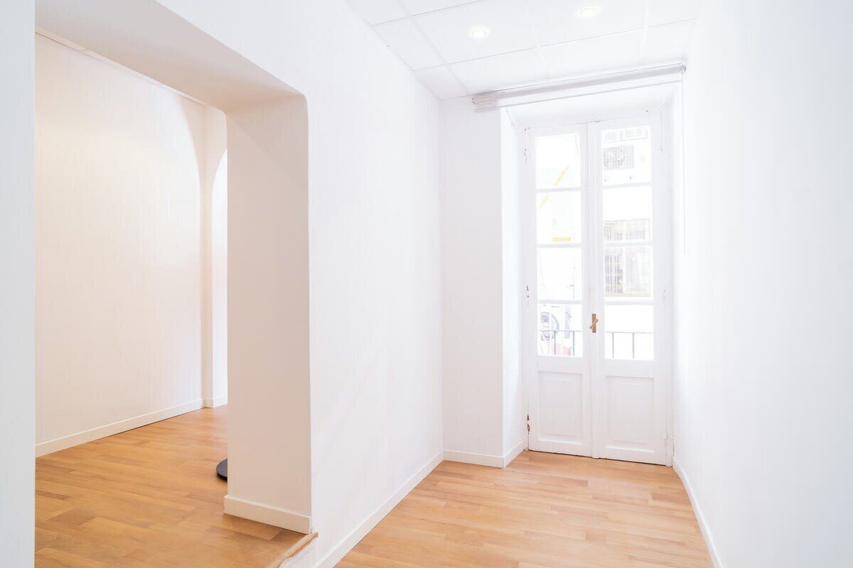 Une pièce aux murs blancs, avec un plancher en bois et une porte blanche.