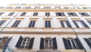 Un immeuble à plusieurs étages, doté de fenêtres en arc de cercle et de volets, de balcons, ainsi que d’une enseigne indiquant la présence d’un restaurant.
