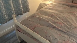 A bedroom with a bed, a nightstand, a lamp, and a window with curtains.