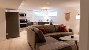 A modern living room with a sectional sofa, a small round table, and a kitchen area with a microwave and stove.