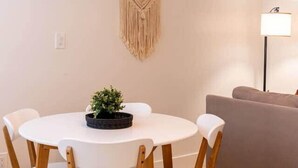 A dining area with a round table, wooden chairs, a macrame wall hanging, and a floor lamp.
