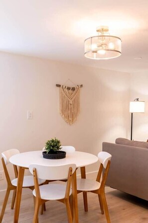 Uma área de refeições com uma mesa redonda, cadeiras de madeira, um pendente de macramé e um abajur.