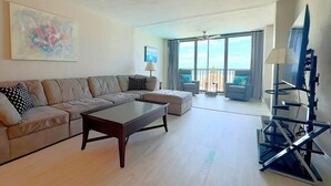 Ein geräumiges Wohnzimmer mit einer Eckcouch, einem Couchtisch und einem Balkon mit Blick.