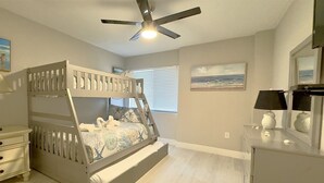 Ein Stockbett mit einer Leiter, eine Kommode, ein Deckenventilator und ein Bild an der Wand.