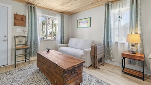 Un salon chaleureux avec un plafond en bois, un canapé, une commode en bois et une lampe posée sur une table d’appoint.