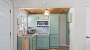 A compact kitchen with teal cabinets, a microwave, and a wooden ceiling.