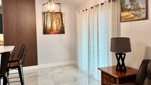 A living room with a wooden dining table, a sofa, a lamp, a painting, and a hanging light fixture.