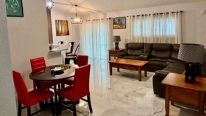 A living room with a sofa, coffee table, and dining area with chairs.