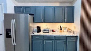 A compact kitchen with teal cabinets, a stainless steel refrigerator, and a marble countertop.