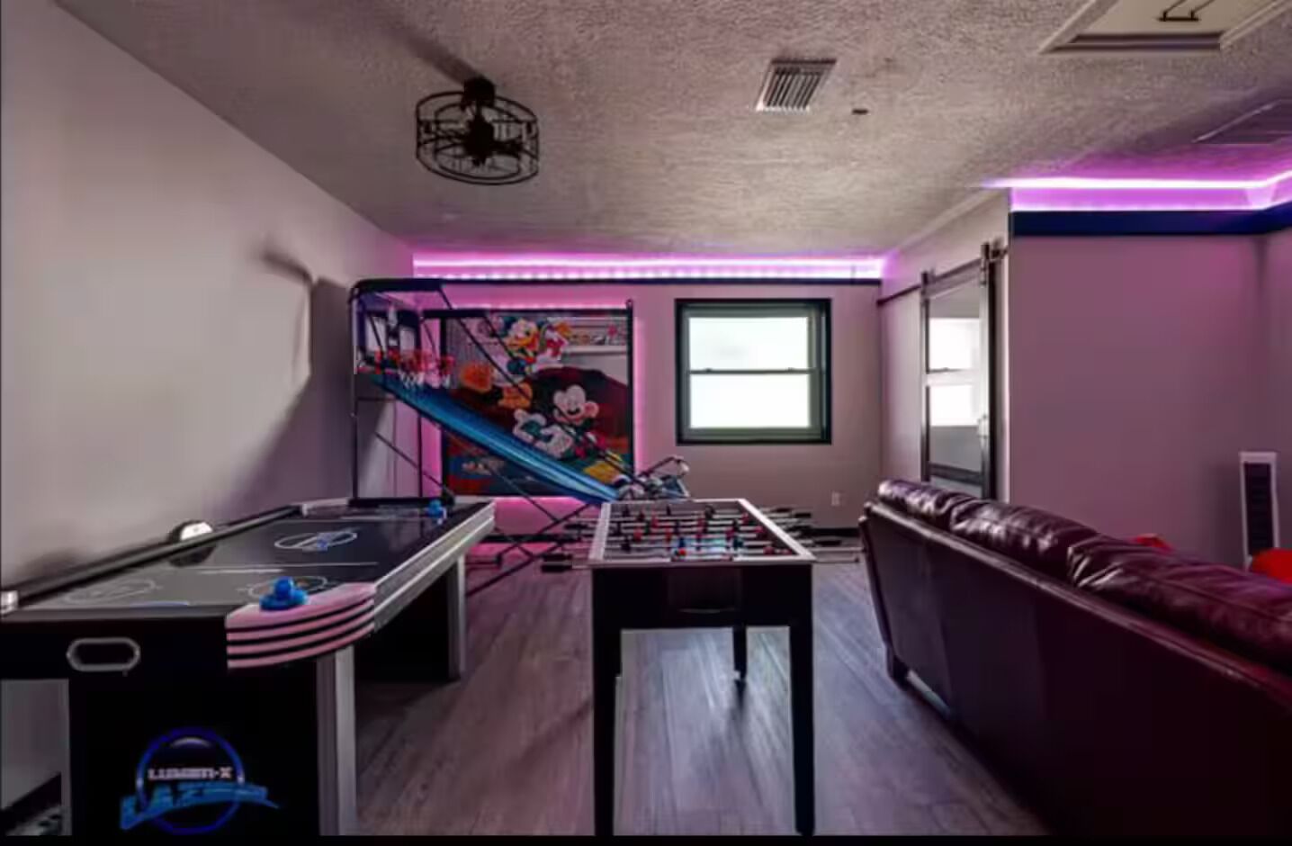 A room with a foosball table, a sofa, a staircase with a cartoon mural, and a window.