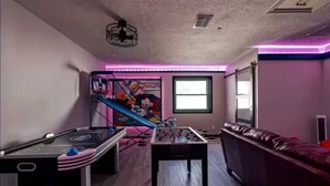 A room with a foosball table, a sofa, a staircase with a cartoon mural, and a window.