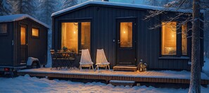 A cabin with a wooden deck, two chairs, a table, and a door leading to an interior space.