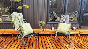 A wooden deck with two chairs and a bench, a candle, and a vase of flowers.