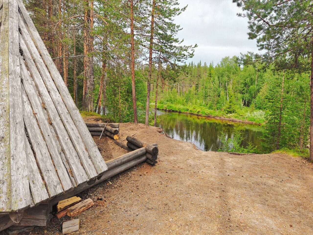 Une construction rustique en bois, située au bord d’un lac paisible, entourée d’une forêt dense.
