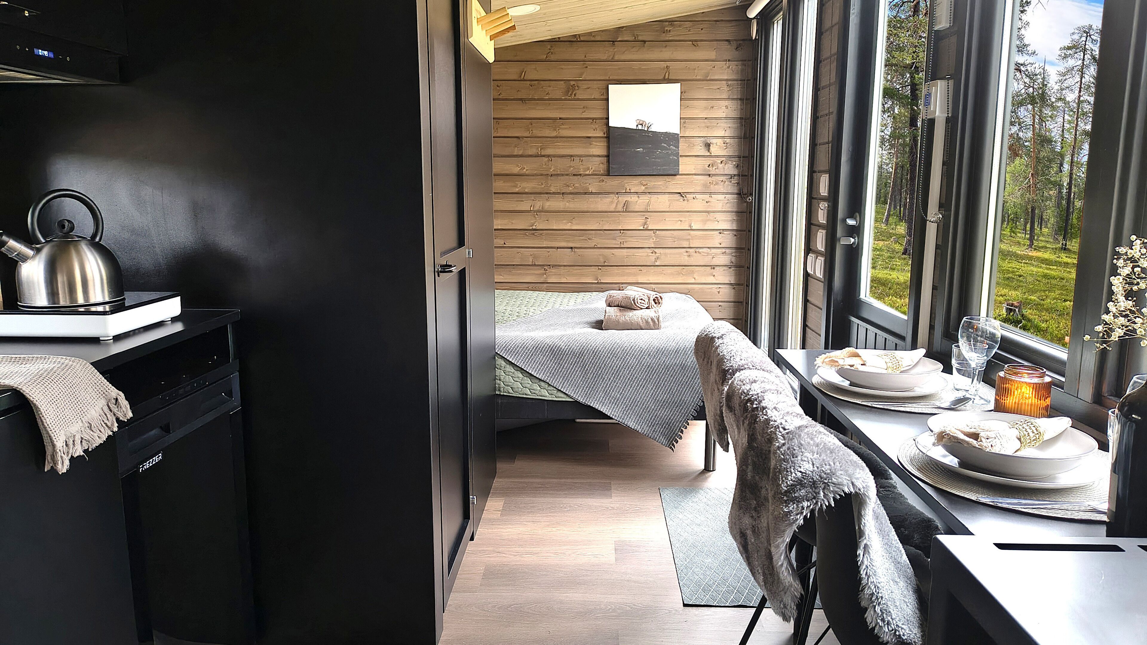 A compact bedroom with a bed, a small table with a candle, and a view of the outdoors.
