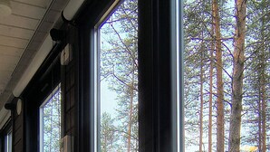 A dining table set with plates, glasses, and a candle in a room with large windows overlooking a forest. - Riverside Village Ylläs (Kolari)
