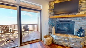 A room with a stone fireplace, a flat-screen TV mounted above it, and a balcony with wooden deck and chairs. - Reserve 36C • Top of the World • Hot Tub (Sugar Mountain)