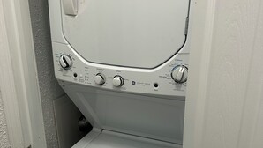 A compact, white washing machine with multiple control knobs and a door handle, situated in a narrow space with a door on one side. - 3-bedroom house in charming Southhull neighborhood, close to downtown! (Montgomery)
