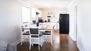 Una cocina moderna con armarios blancos, un refrigerador negro y un comedor con sillas y una mesa blancos.