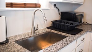 Una cocina con un lavamanos de acero inoxidable, un microondas y una bandeja negra sobre la encimera.