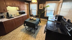 A compact kitchen with dark walls, a ceiling fan, a microwave, a coffee maker, and a dining table with a basket. - Gallows Hill Guest House, Charming 2BR Apartment on Gallows Hill in Salem, MA (Salem)
