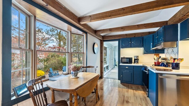 A kitchen with wooden beams, blue cabinets, a dining table with chairs, and a view of the outdoors.