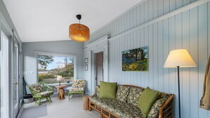 A cozy room with a wooden sofa, green cushions, a wicker chair, and a painting on the wall.