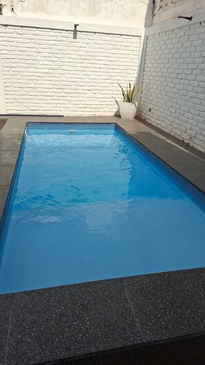 A rectangular swimming pool with a dark edge, surrounded by a white brick wall and a potted plant.