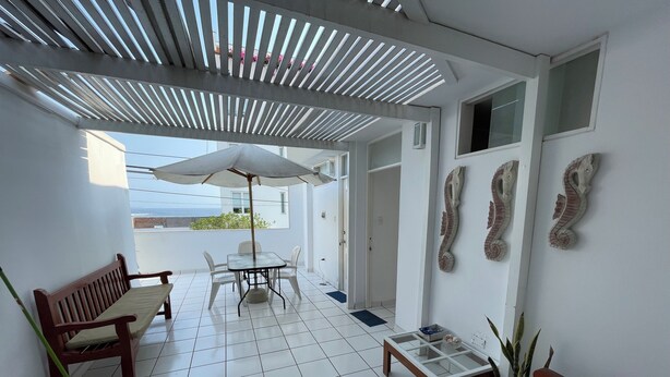 A clean, modern patio with a tiled floor, a wooden bench, a table with chairs, and a ceiling with slatted design. - Cozy Room w/ Private Bath + Shared Kitchen 5 Min to Beach -Surf Hostel Vibe (San Miguel)