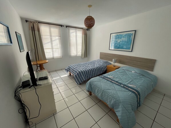 Un dormitorio con dos camas, un escritorio con computadora, una silla y una ventana con cortinas.