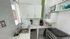 A modern kitchen with white cabinets, a stainless steel sink, a coffee maker, and a stove. - Cozy Room w/ Private Bath + Shared Kitchen 5 Min to Beach -Surf Hostel Vibe (San Miguel)