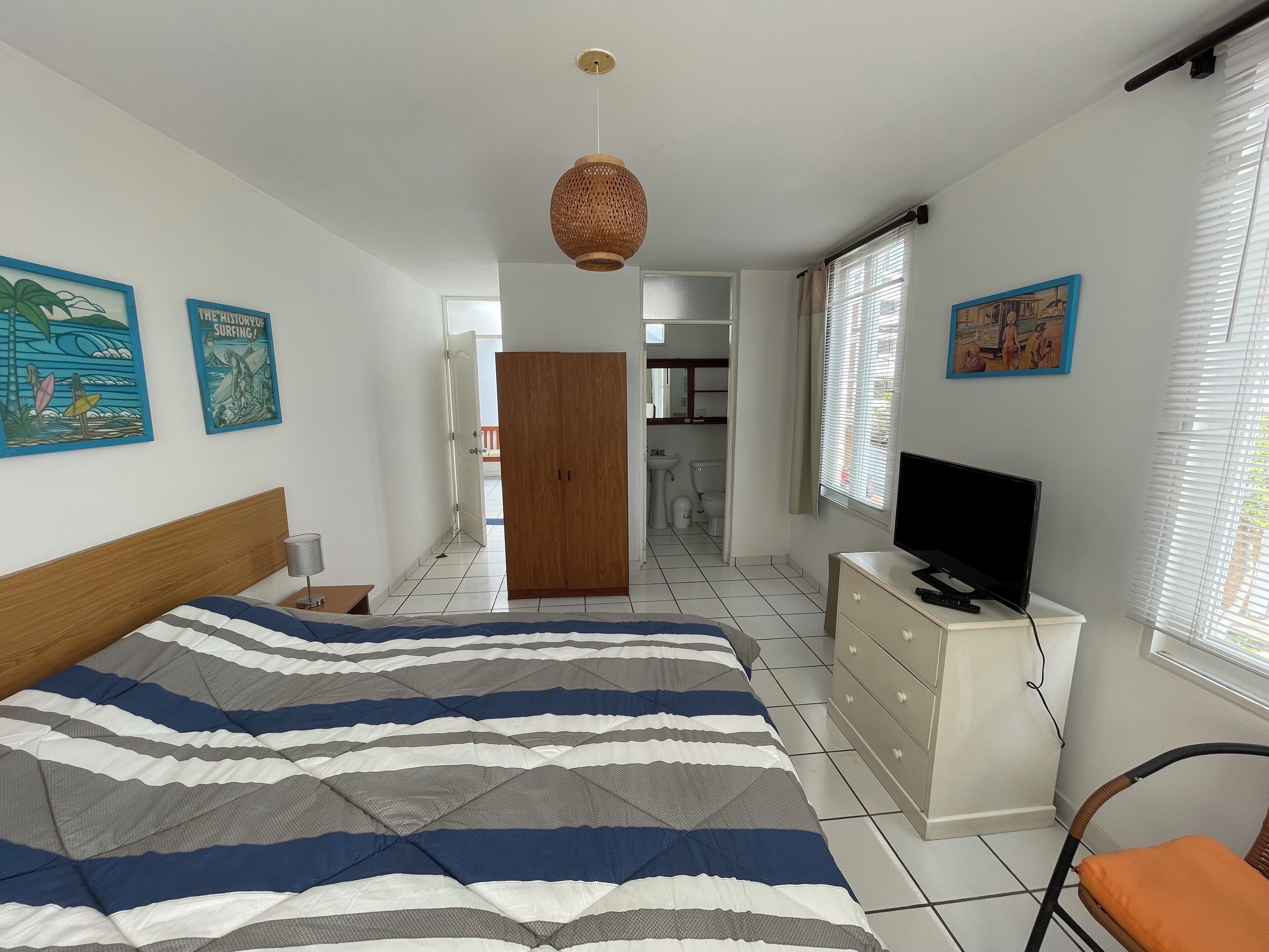 Un dormitorio con cama, televisión, cómoda y obras de arte en las paredes.