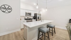 Una cocina moderna con armarios blancos, una isla central, taburetes de bar e iluminación colgante.