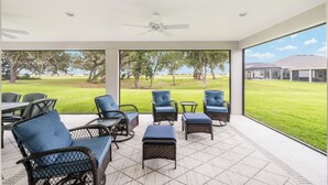Un patio techado con mobiliario de mimbre y vista a una zona verde.